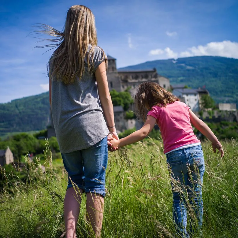 Deux enfants marchent dans l’herbe face au château de Valère